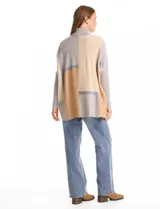 Polera tipo poncho de corte oversize, con cuello alto tejido y mangas largas con puños elásticos. Presenta un diseño geométrico de bloques de color en tonos beige, gris y tostado.