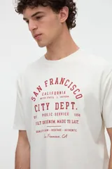 Remera de manga corta color blanco con estampa tipográfica frontal en tono rojo, de calce clásico y cuello redondo.