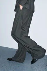 Pantalón de tiro medio con diseño de pierna ancha y pinzas frontales. Cuenta con cintura con trabillas, bolsillos laterales ocultos y cierre frontal con cremallera, botón y ganchos metálicos.