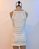 Vestido corto blanco de tejido de punto con cuello halter y diseño calado en la parte superior y en franjas horizontales a lo largo de la falda ajustada.
