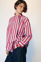Camisa de manga larga con cuello subido y detalle de lazada frontal. Presenta un diseño de rayas verticales en tonos verde y celeste, con cierre frontal de botones y puños clásicos.