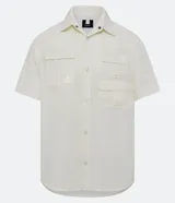 Camisa color crema de corte oversized, con cuello inglés, manga corta y cierre frontal abotonado. Presenta múltiples bolsillos tácticos delanteros.