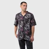 Camisa de manga corta con cuello cubano, confeccionada en viscosa suave y ligera. Presenta un estampado botánico de hojas en tonos violeta, gris y blanco sobre una base negra. Incluye un bolsillo frontal en el pecho y cierre con botones.