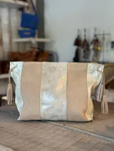 Sobre de cuero combinado en tonos beige y dorado metalizado, con diseño de paneles verticales y borlas colgantes en los laterales.