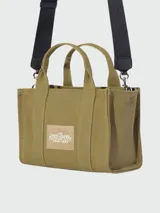 Bolso tipo tote de Marc Jacobs, confeccionado en lona resistente color beige. Presenta el logo estampado en contraste en el frente, doble asa superior y cierre superior con cremallera.
