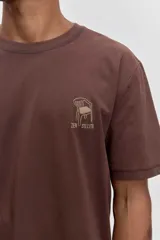 Remera de algodón color marrón chocolate, de corte clásico y cuello redondo, con un pequeño estampado gráfico en el pecho.