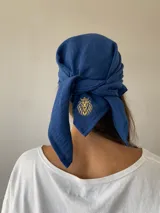 Conjunto compuesto por un pareo corto de color azul con detalle de bordado dorado en el frente y una bandana a juego. El pareo cuenta con un diseño envolvente con lazo lateral.