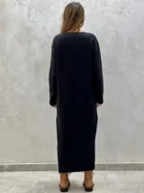 Vestido midi de punto color azul marino, con cuello en V, mangas largas y diseño holgado. Presenta un patrón de rombos en relieve y aberturas laterales con botones decorativos en el ruedo.