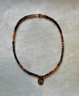 Collar de cuentas facetadas de piedras naturales multicolor con dije dorado ovalado en forma de sol con una piedra central.