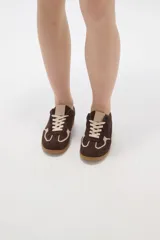 Zapatilla urbana de gamuza color marrón con detalles en beige, cordones claros y suela de goma tipo caramelo.