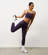 Top deportivo de microfibra en color violeta con detalles de friso en tono arena. Presenta un diseño de escote redondo, breteles finos y una banda inferior elástica que proporciona mayor sujeción. Incluye copas removibles para mayor comodidad.