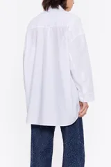 Camisa larga blanca de algodón, de corte recto, con cuello camisero, manga larga, puños con botones, cierre frontal de botonadura y bolsillo de plastrón en el pecho con logo en relieve.