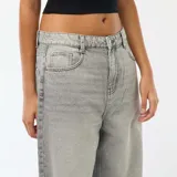 Jean de corte baggy y tiro bajo, color gris con efecto lavado y detalles de roturas en las piernas. Cuenta con diseño clásico de cinco bolsillos y cierre frontal con botón y cremallera.
