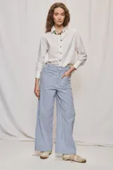 Pantalón de pierna ancha y tiro medio con diseño de rayas verticales blancas y azules. Cuenta con bolsillos delanteros amplios y cierre frontal con botón y cremallera.