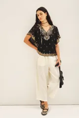Blusa de gasa negra con escote en V, mangas amplias de largo irregular y bordados detallados con canutillos, lentejuelas y mostacillas. Incluye viso al tono con breteles regulables.