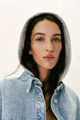 Cazadora de denim oversize con capucha gris desmontable, cuello camisero, cierre frontal con botones metálicos y bolsillos delanteros de plastrón.