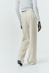 Pantalón gris de tiro alto con bolsillos delanteros y traseros, detalle de pliegues frontales y cierre frontal con cremallera y botón.