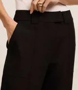 Pantalón de vestir negro, estilo carrot (holgado en cadera y ajustado en tobillo), de cintura alta con trabillas y cierre tradicional. Presenta recortes verticales con costura aparente en el frente.