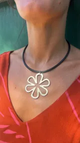 Collar de tiento de cuero negro con un dije de alpaca calado en forma de flor de seis pétalos.