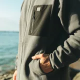 Canguro de micropolar gris con cierre frontal completo, capucha negra y bolsillo frontal con cierre en contraste negro. Presenta un diseño funcional y térmico con acabado suave.