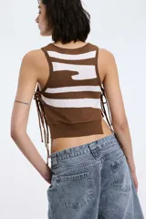 Top crop tejido de punto sin mangas, con diseño bicolor en blanco y negro de franjas y detalles de lazos laterales.