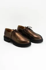 Wallabee de cuero metalizado en tono bronce, con cordones al tono y suela track de goma negra con plataforma.
