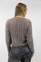 Buzo de chenille color blanco, con cuello redondo, mangas largas y diseño tejido con trenzas verticales en el frente y las mangas. Cuenta con terminaciones acanaladas en el cuello, los puños y la cintura.
