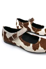 Zapato Mary Janes de cuero con estampado de vaca en tonos marrón y blanco, con correa sobre el empeine y hebilla metálica.