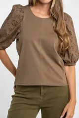 Remera de algodón color rosado con mangas cortas abullonadas de broderie con diseño floral calado. Presenta cuello redondo y costura vertical central en el frente.