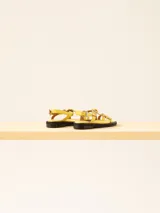 Sandalia baja de cuero vacuno con tiras cruzadas y aplique decorativo. Tiene hebilla en el talón y empeine para regular el calce.