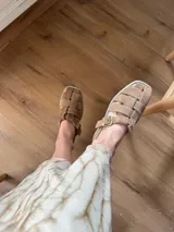 Sandalias de cuero marrón con diseño de tiras entretejidas y hebilla lateral.