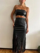 Falda midi negra de cuero sintético, corte ajustado y flecos largos en el ruedo.