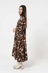 Vestido midi de corte holgado con estampado animal print en tonos marrones y beige. Tiene cuello redondo con lazo, mangas largas abullonadas y falda amplia con volantes. Incluye cinturón marrón con tachas.