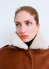Chaqueta estilo aviador de cuero sintético marrón, con cuello de corderito sintético blanco, bolsillos frontales con solapa, cierre de cremallera y puños y cintura de canalé elástico.