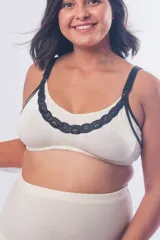 Top maternal de algodón color crudo, sin aros, con detalles de puntilla negra en el escote. Cuenta con breteles elásticos regulables con clip para lactancia y cierre de broches en la espalda.