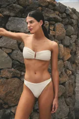 Conjunto de bikini color hueso, confeccionado en lycra texturada. El corpiño es strapless con tiras ajustables y hebilla metálica en el centro. La bombacha es vedetina y está forrada.
