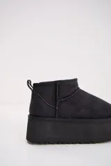 Bota corta tipo ugg de color negro, con plataforma alta y suela dentada. Presenta costuras reforzadas y tirador en la parte trasera.