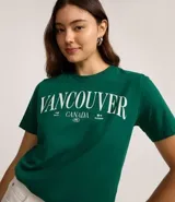 Remera de algodón color verde esmeralda con cuello redondo y mangas cortas. Presenta un estampado frontal en blanco con el texto "VANCOUVER CANADA".