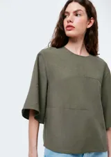Blusa de manga corta color verde oliva, con cuello redondo y diseño de paneles con costuras visibles. Presenta un corte holgado y mangas con caída amplia.