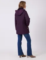 Campera capitoneada de largo midi en color bordó, con diseño de rombos en el cuerpo y mangas, y costuras diagonales en los laterales. Cuenta con cierre frontal, capucha desmontable con interior suave y panel entallado en la cintura.