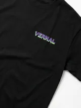 Remera negra de algodón premium con corte relajado. Presenta un diseño gráfico estampado en la espalda que combina tonos violeta y verde ácido, con una ilustración conceptual de un rostro y elementos abstractos.