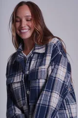 Sobrecamisa de franela color beige con estampado a cuadros en tonos marrones y azules, de corte holgado, con cuello clásico, cierre abotonado y bolsillos delanteros con solapa.