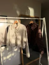 Chaqueta corta de color marrón con diseño acolchado de rombos, cuello camisero y cierre frontal con botones a presión.