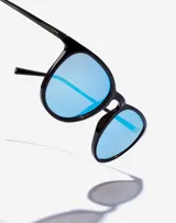 Gafas de sol Hawkers unisex, modelo Ollie, con montura negra redonda y lentes espejadas celestes.