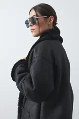Tapado de efecto cuero negro con interior y detalles de cuello y puños en pelo sintético. Presenta un diseño envolvente con cierre frontal de botones y bolsillos laterales.