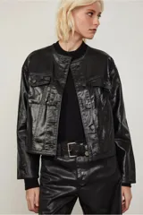 Campera negra efecto vinilo con terminación brillante y cuello redondo acanalado. Presenta bolsillos con solapa en el frente, costuras marcadas y cierre con broches a tono.