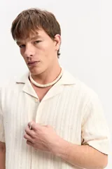 Camisa de manga corta color beige con tejido calado de líneas verticales y cuello abierto estilo resort.
