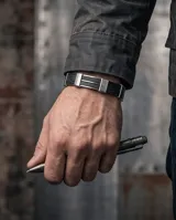 Pulsera de diseño moderno compuesta por una banda central de goma negra flanqueada por piezas de acero inoxidable con grabado de guarda griega.