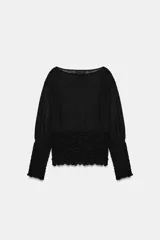 Jersey de punto semitransparente negro, con cuello redondo y mangas largas. Presenta detalles de nido de abeja elástico en los puños y en el cuerpo.