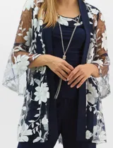 Conjunto de tres piezas compuesto por una musculosa de silueta recta, un pantalón de seda fría con caída fluida y cintura elastizada, y un kimono de tul con bordado floral, frente abierto y mangas acampanadas. Incluye collar largo removible.
